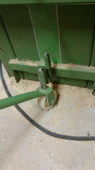 Hjul på en grönmålad metallkonstruktion mot en betonggolv och en grön container.