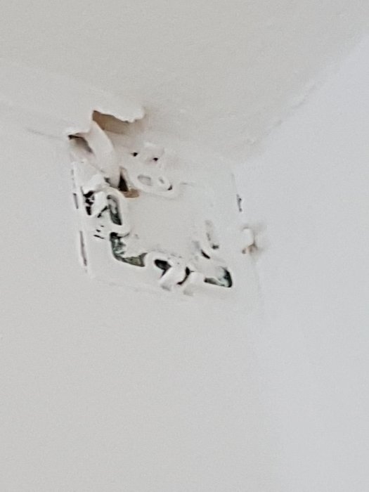 Skadad gipsskiva och eluttag med bortskalad färg och synliga ledningar i taket.