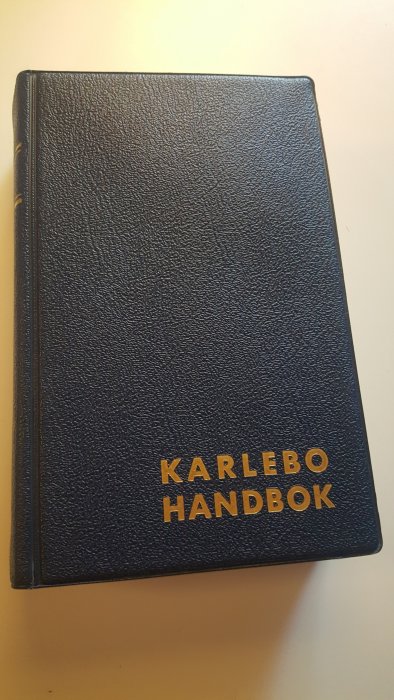 Blå bok med titeln "KARLEBO HANDBOK" i gula bokstäver på framsidan.