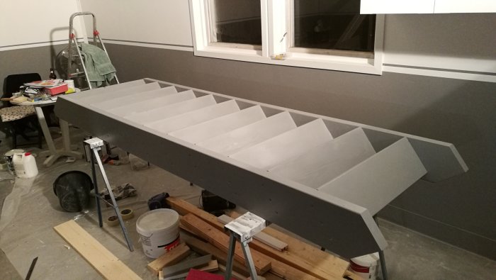 Nymålad grå trappa på pallbockar i ett rum under renovering med verktyg och målarföremål runtomkring.