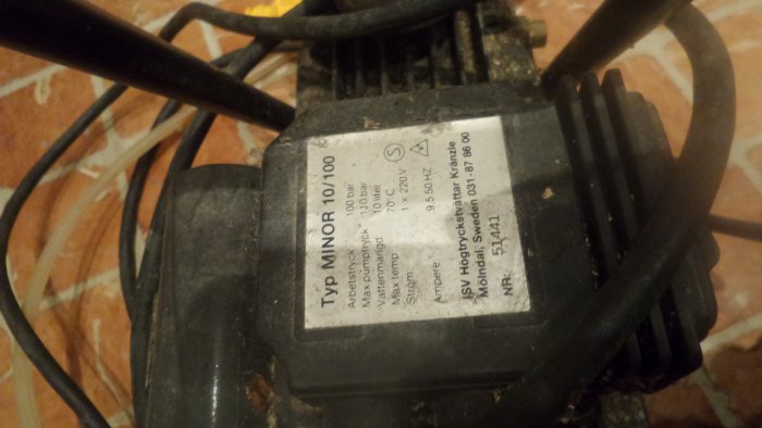 Närbild på en etikett för en elektrisk enhet, förmodligen pump, med tekniska specifikationer, placerad på ett golv.