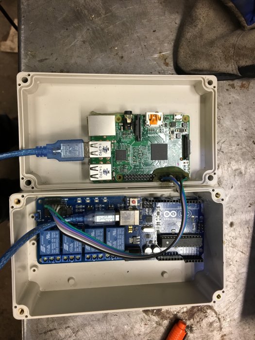 Raspberry Pi och reläkort monterade i en vit elektroniklåda, med nätverkskabel och ledningar anslutna.