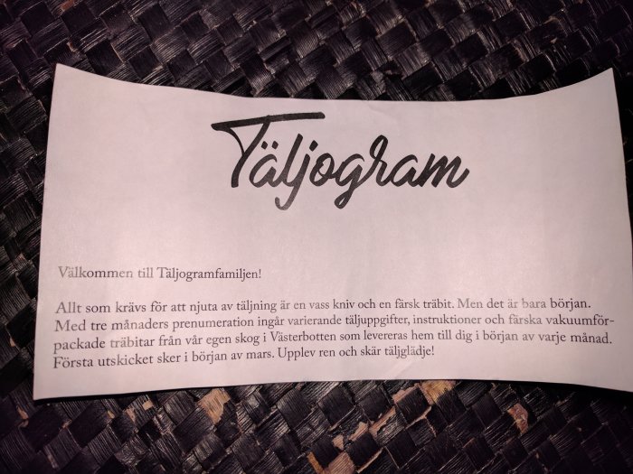 Pappersblad med texten "Täljogram" och välkomsthälsning till en prenumerationstjänst för täljning med träbitar och instruktioner.