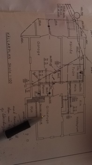 Ritning över källarplan med anteckningar och penna som pekar, planer för renovering.
