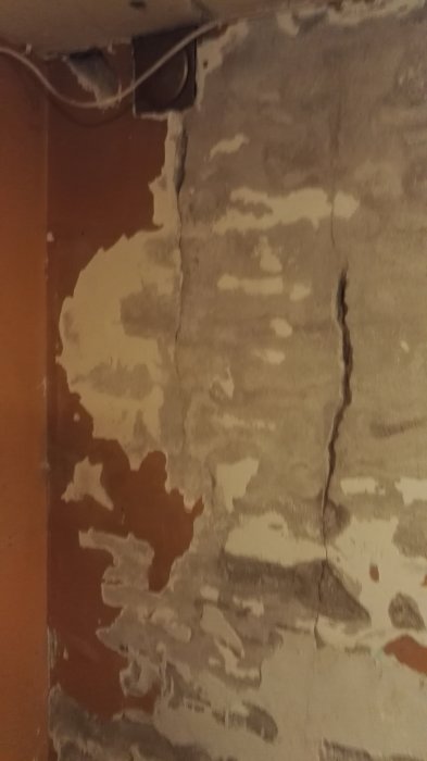 Vertikal spricka i fasad med delvis borttaget ytskikt som exponerar underliggande lager.