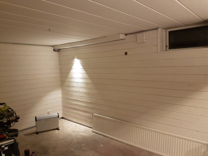 Målad garageinteriör med elektrisk installation och upplyst av en lampa.