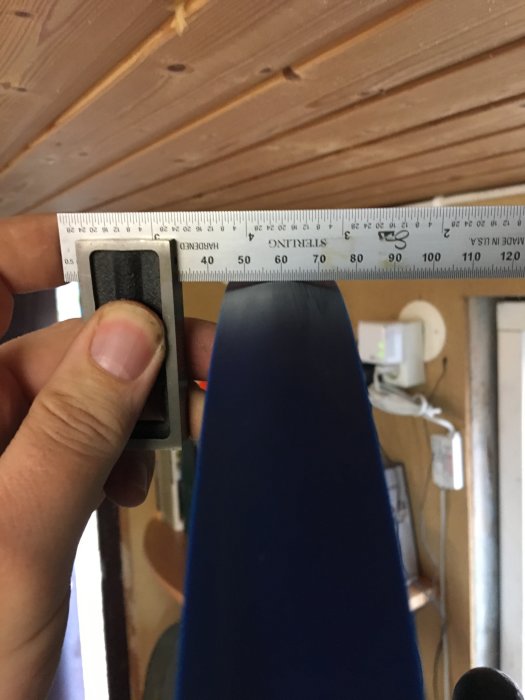 Hand håller ett måttband mot en nyinstallerad blå maskindel för att kontrollera position.