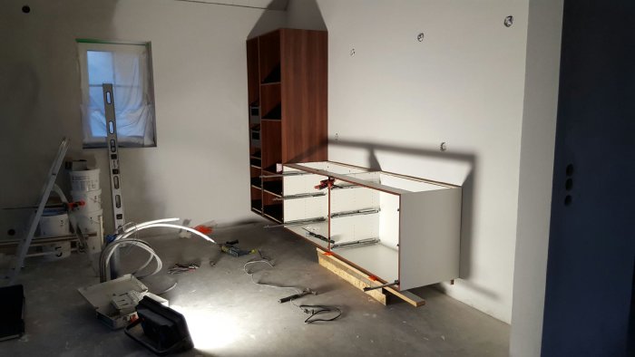 Köksrenovering i process med installation av vita och valnötsfärgade skåp och konstruktionsmaterial på golv.