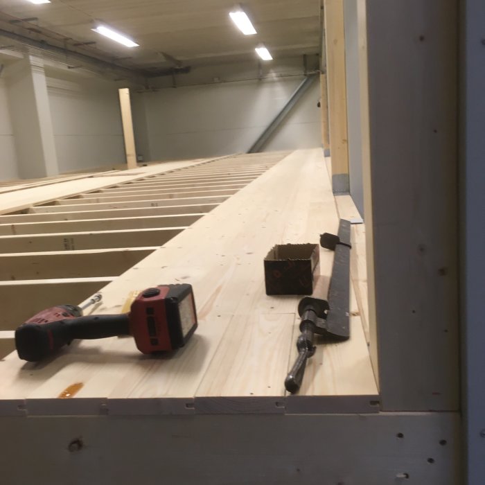 Träbjälklag för lagerloft under konstruktion med borr och skruvar på plankgolv.