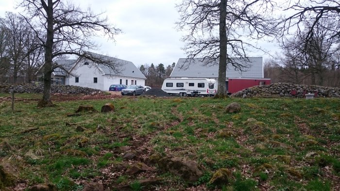 Husvagn parkerad vid boningshus på landet med stenmur och grönt fält i förgrunden.