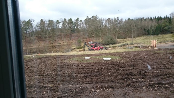 Grävmaskin som arbetar med markarbete utomhus, omgivet av skog och gräs.