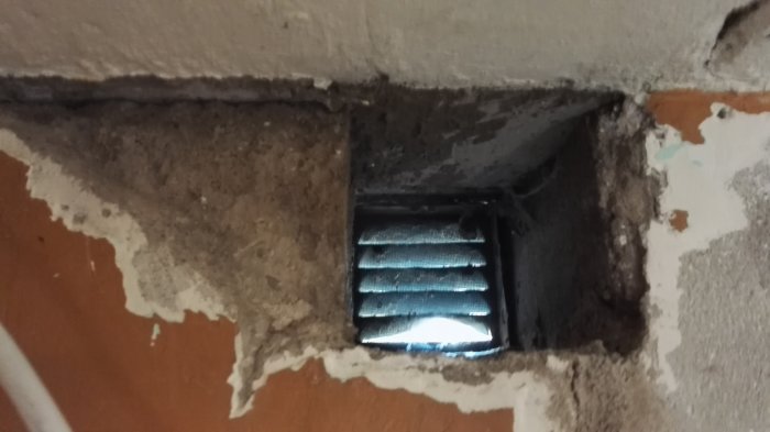 Reparerad grundvägg där ett värmeelement avlägsnats, med synligt hål och ett ventilationsgaller.