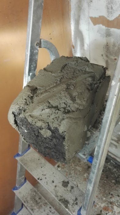 Fräsch våt puts applicerad på yttre hörn av byggelement med stegstege i bakgrunden.