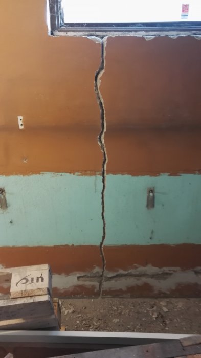 En spricka i en tegelvägg under renovering med delvis avlägsnad puts och ett fönster ovanför.