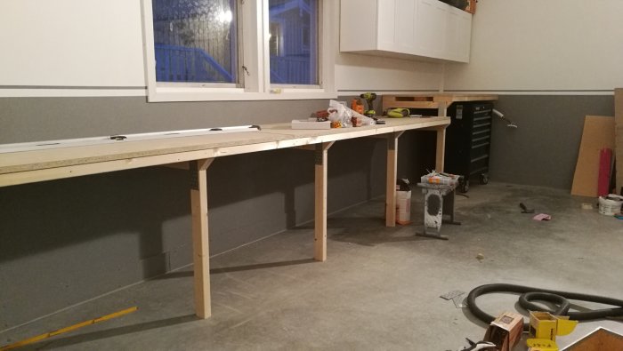 Nybyggd arbetsbänk i ett garage med verktyg och en monterad trappa i bakgrunden.