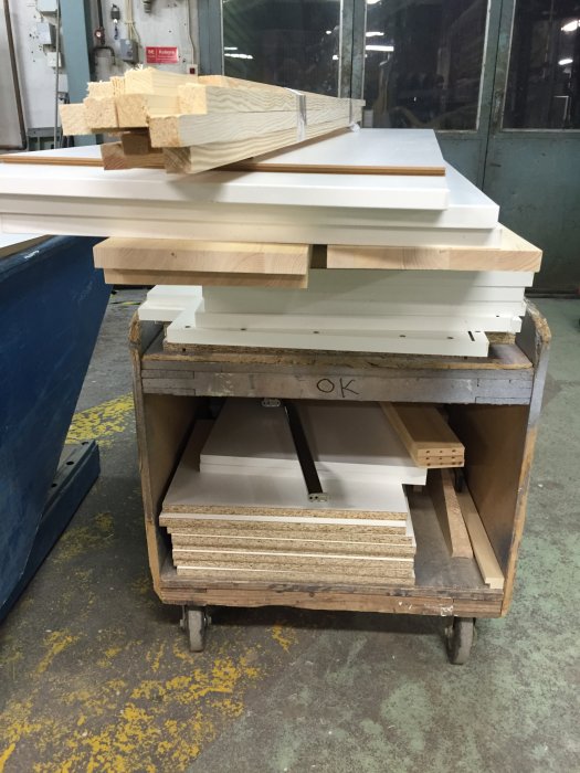 Uppskurna melaminbelagda spånskivor och trädetaljer staplade på en vagn i ett snickeri, redo för montage.