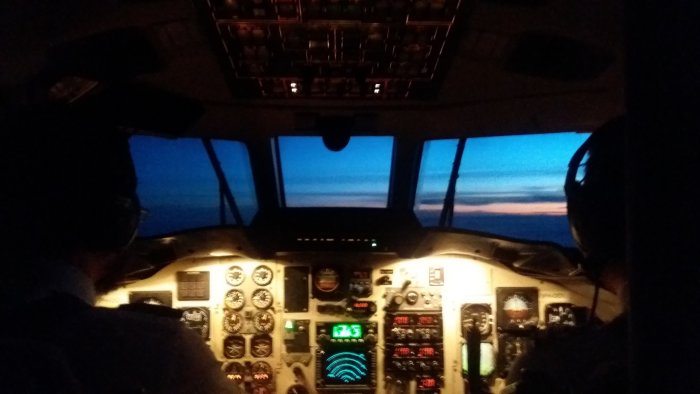 Vy från ett flygplans cockpit med piloter och instrumentbräda under flygning i skymningen.
