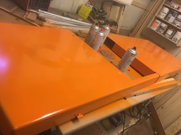 Nyomålad orange arbetsbänk med sprayburkar på toppen i en verkstad.