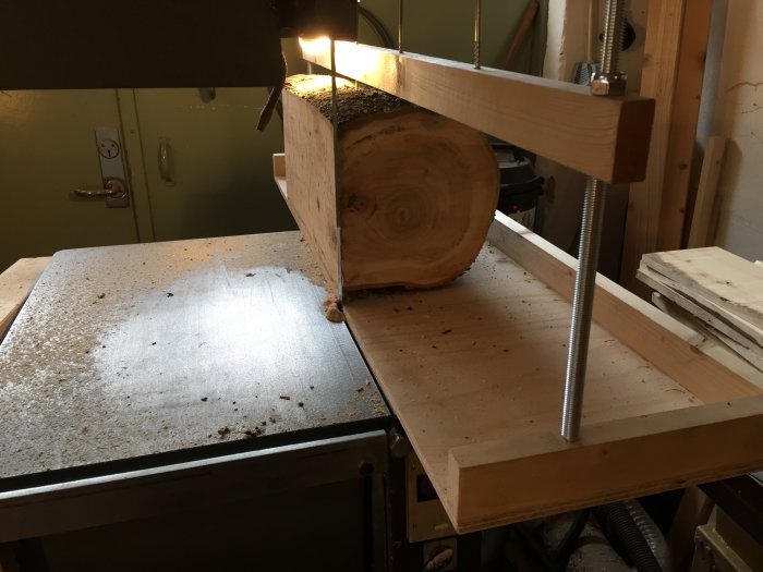 Trästock fastklämd i en hemmagjord träbearbetningsanordning med genomgående skruvar.