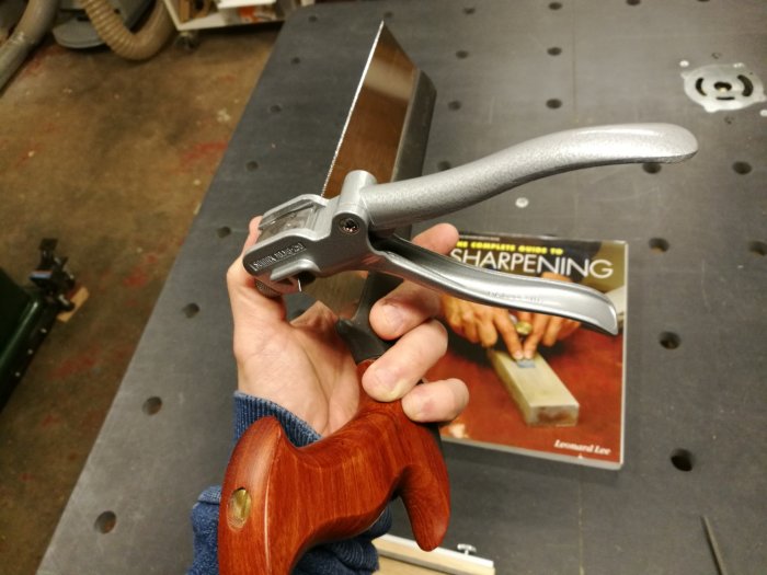 Hand håller en skränktång för sågtänder och en bok om slipning i bakgrunden.