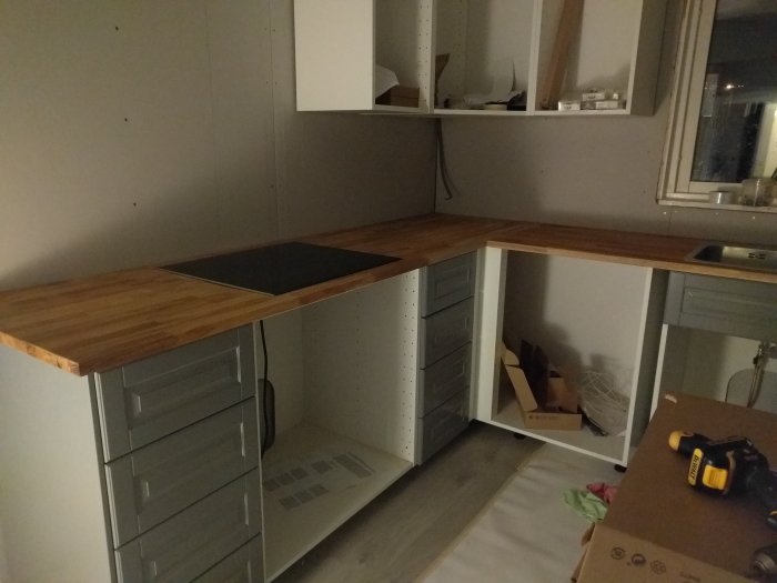 Nyinstallerade bänkskivor med diskho och induktionshäll, och halvmonterade skåpslådor i ett kök under renovering.