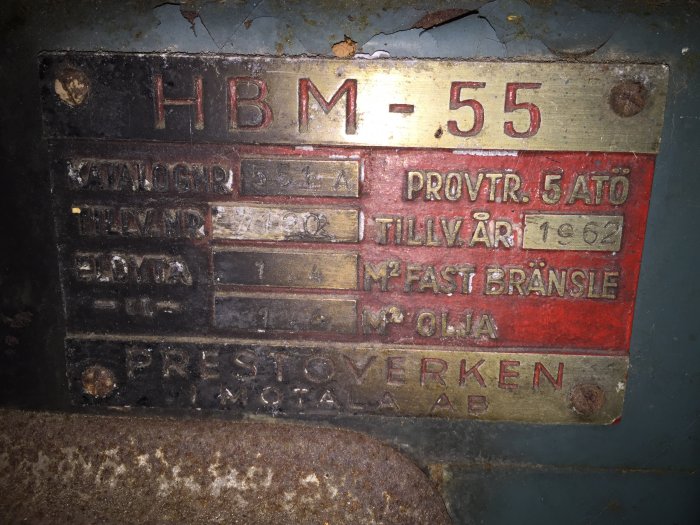 Gammal metallskylt på en värmepanna med texten 'HBM-55', 'Tillv. år 1962', och 'Prestoverken AB'.