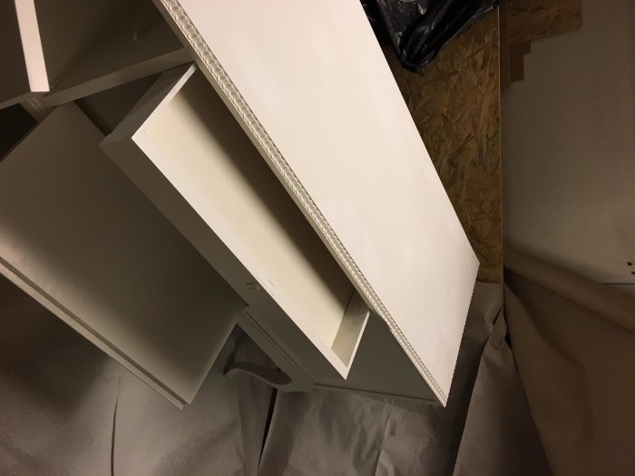 Vitmålad trämöbel med synlig blödning genom lackfärg, upplagd på skyddspapper.