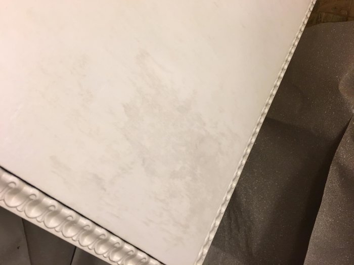 Målad vit möbelyta med synliga blödningar av träfärg genom vit färg och detalj av dekorativ kant.