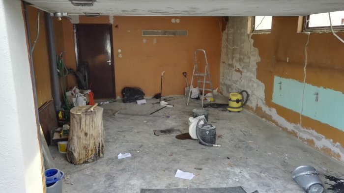 Tomt garage med spacklade väggar och renoveringsmaterial på golvet.
