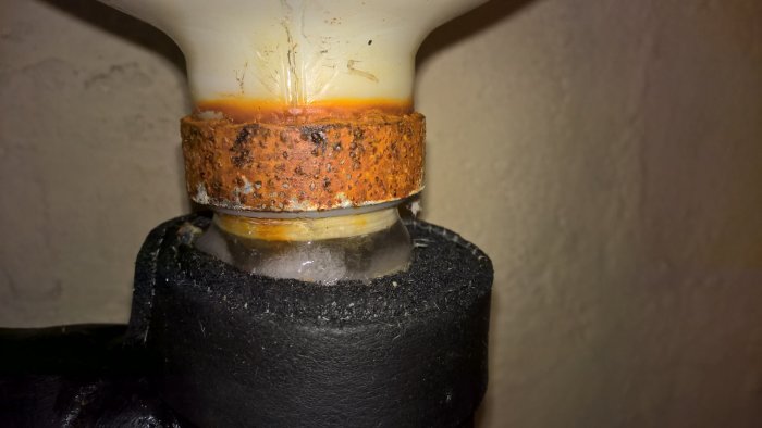 Rostigt rörkoppling och isolering med fuktindikationer, troligen nära ett expansionskärl i ett värmesystem.