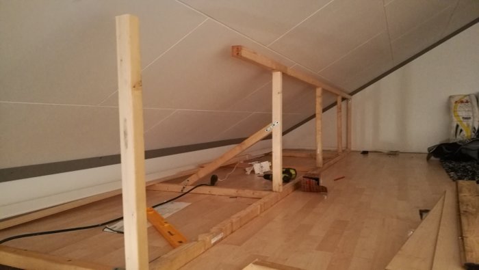 Pågående bygge av trähyllor för förvaring längs snedtaket på ett loft.