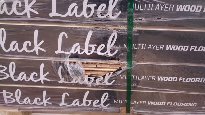 Skadade förpackningar med trägolv märkta "Black Label Multilayer Wood Flooring".