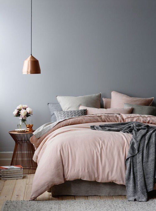 Sovrumsinredning med gråa väggar och sängkläder i rosa och grått toner samt en kopparfärgad lampa.