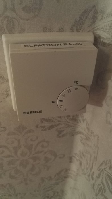 Termostat märkt med "ELPATRON PÅ/AV" och temperaturinställning, monterad på vägg med tapeter.