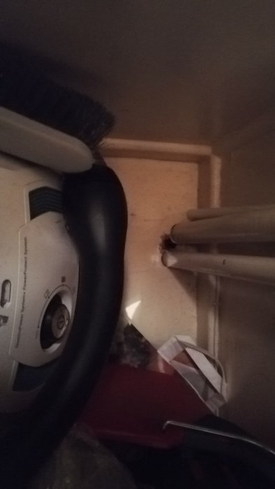 Rör i en vrå vid ett fönster, nära en termostat och olika föremål, möjlig fråga om värmeinställningar.