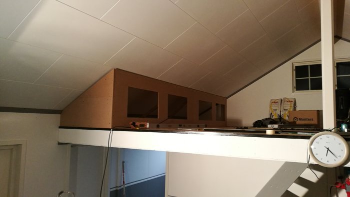 Obyggd förvaringshylla under snedtak med öppna fack och verktyg ovanpå.