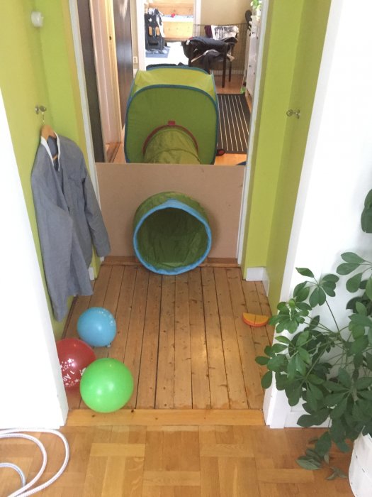 Barnsäkrat hem med lektunnel och barriär i korridor, färgglada ballonger på trägolvet.