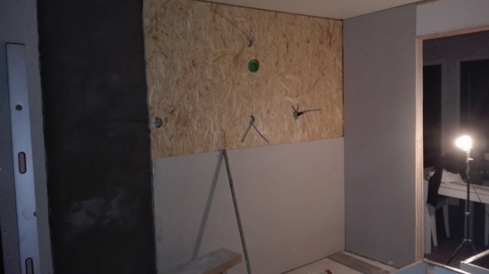 Vägg under renovering med OSB-skiva, putsad murstock och gipsskiva vid sidan.