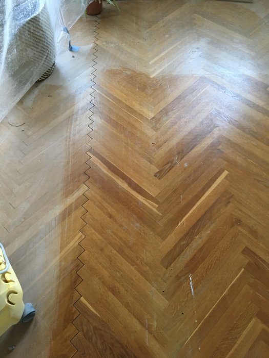 Delvis täckt herringbone-parketgolv under renovering med skarp övergång där nytt stycke möter gammalt golv.