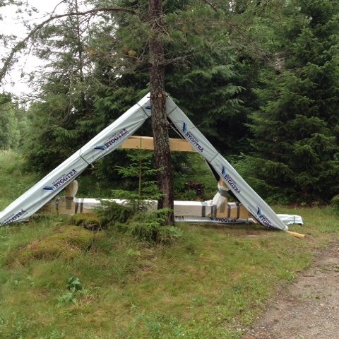 Materialleverans från Nordiska Byggträ för stugbygge med takstolar ute på gräsmatta.