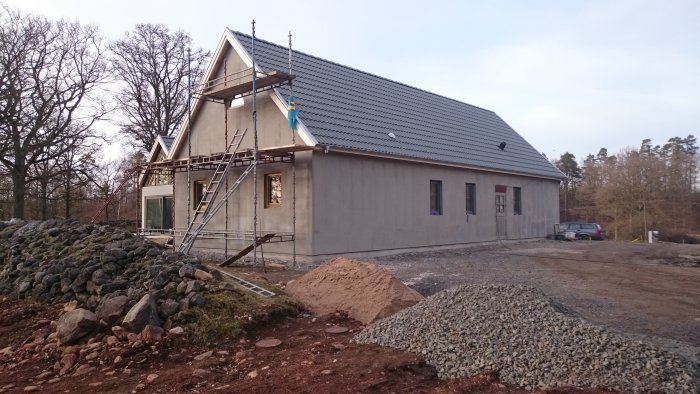 Hus under renovering med pågående putsarbete och byggställningar runt fasaden, intill en grushög.