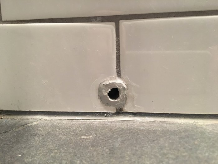 Ett skvallerrör i ett badrum med synlig plastkabel och våtrumssilikon applicerat runt rörets hål i väggen.