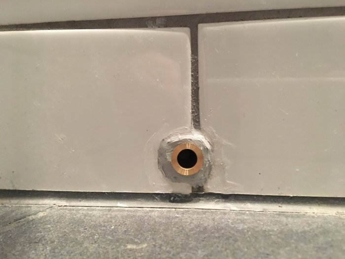 Synlig plastkabel i skvallerrör täckt med våtrumssilikon omringad av vita kakelplattor.