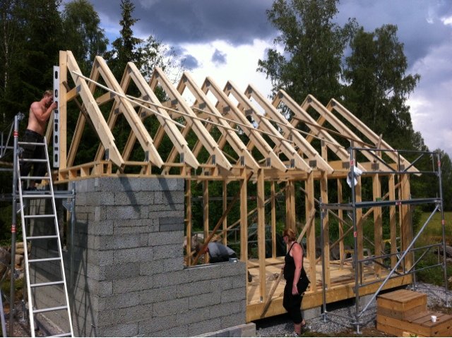 Byggställning vid konstruktion av takstolar över en husgrund med grå lecablock och träreglar.