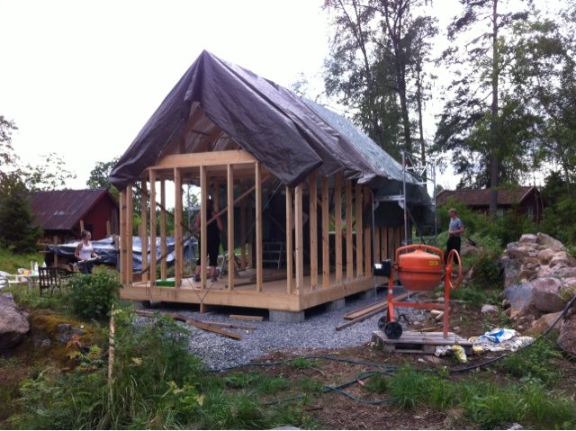 Byggställning och träreglar på ett hus under uppbyggnad med presenning som skydd mot väder.