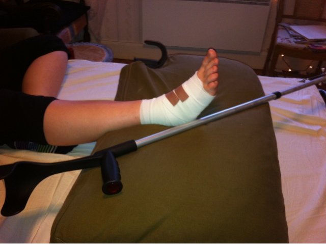 Fot i gips och kryckor efter byggrelaterad olycka, ligger på en soffa med grön dyna.