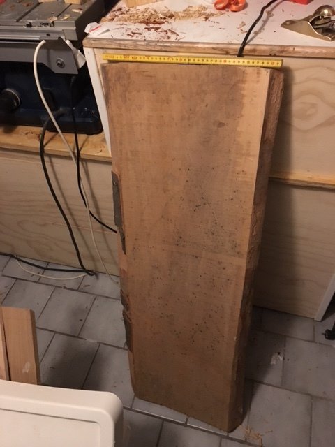 En lång och tung träplanka står på ett golv med en måttband på ovansidan, misstänkt att vara av mahogny.