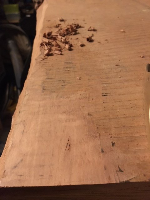Hyvlad träplanka med spån, möjligtvis mahogny, på arbetsbänk.