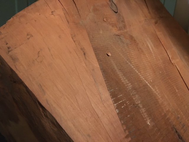 Grovsågad träplanka med rödbrun färg, möjligtvis mahogny, med synliga sågmärken och textur.