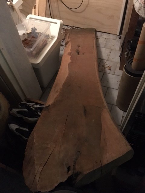Lång, ohyvlad planka av trolig mahogny som är lagrad inomhus, bred och med råa kanter.